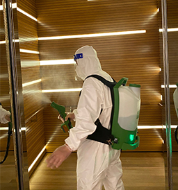 IK Services personnel in protective gear spraying disinfectant in a room