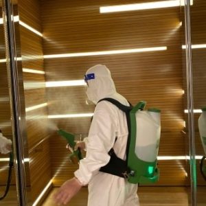 IK Services personnel in protective gear spraying disinfectant in a room