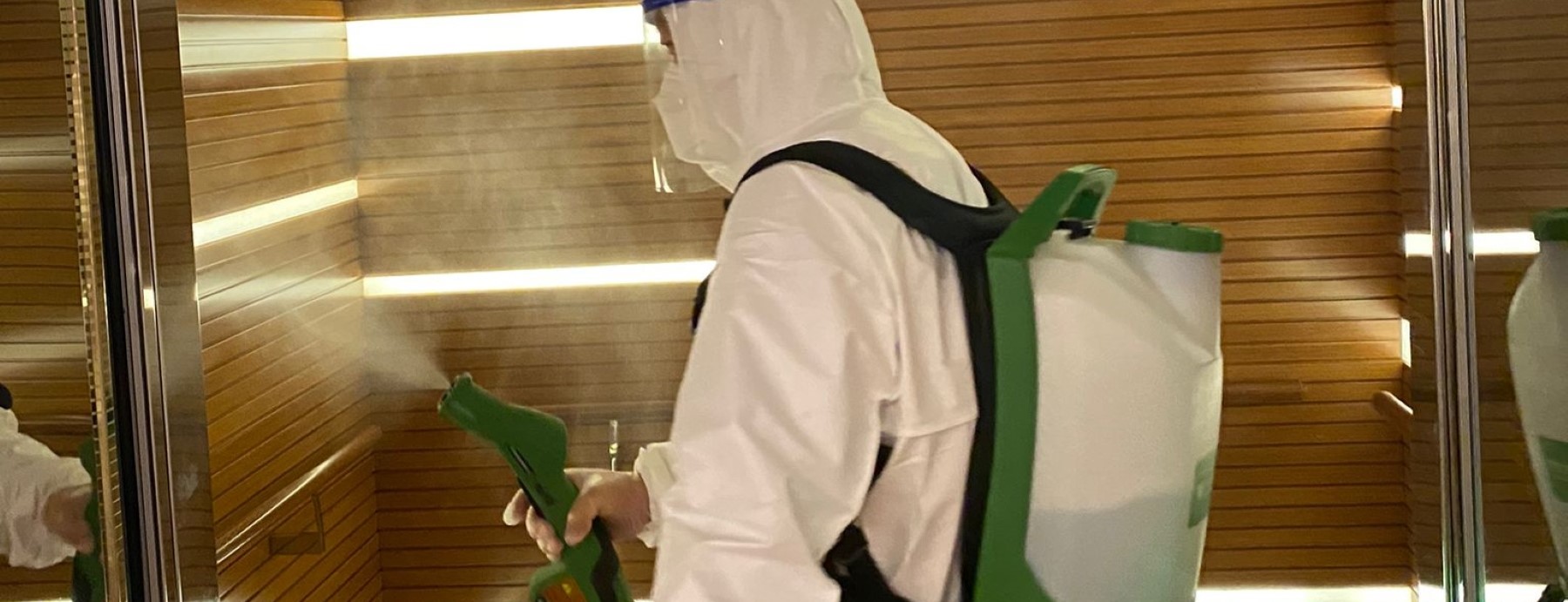 IK Services personnel in protective gear spraying disinfectant in a room